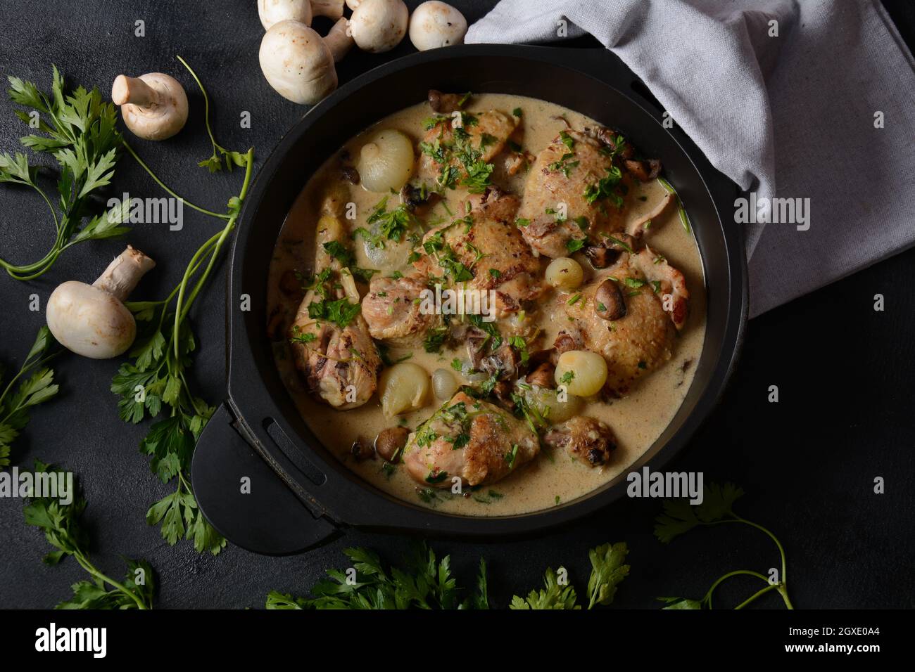 Fricassee - cuisine française. Poulet cuit dans une sauce crémeuse aux champignons dans un four hollandais noir sur une table noire Banque D'Images