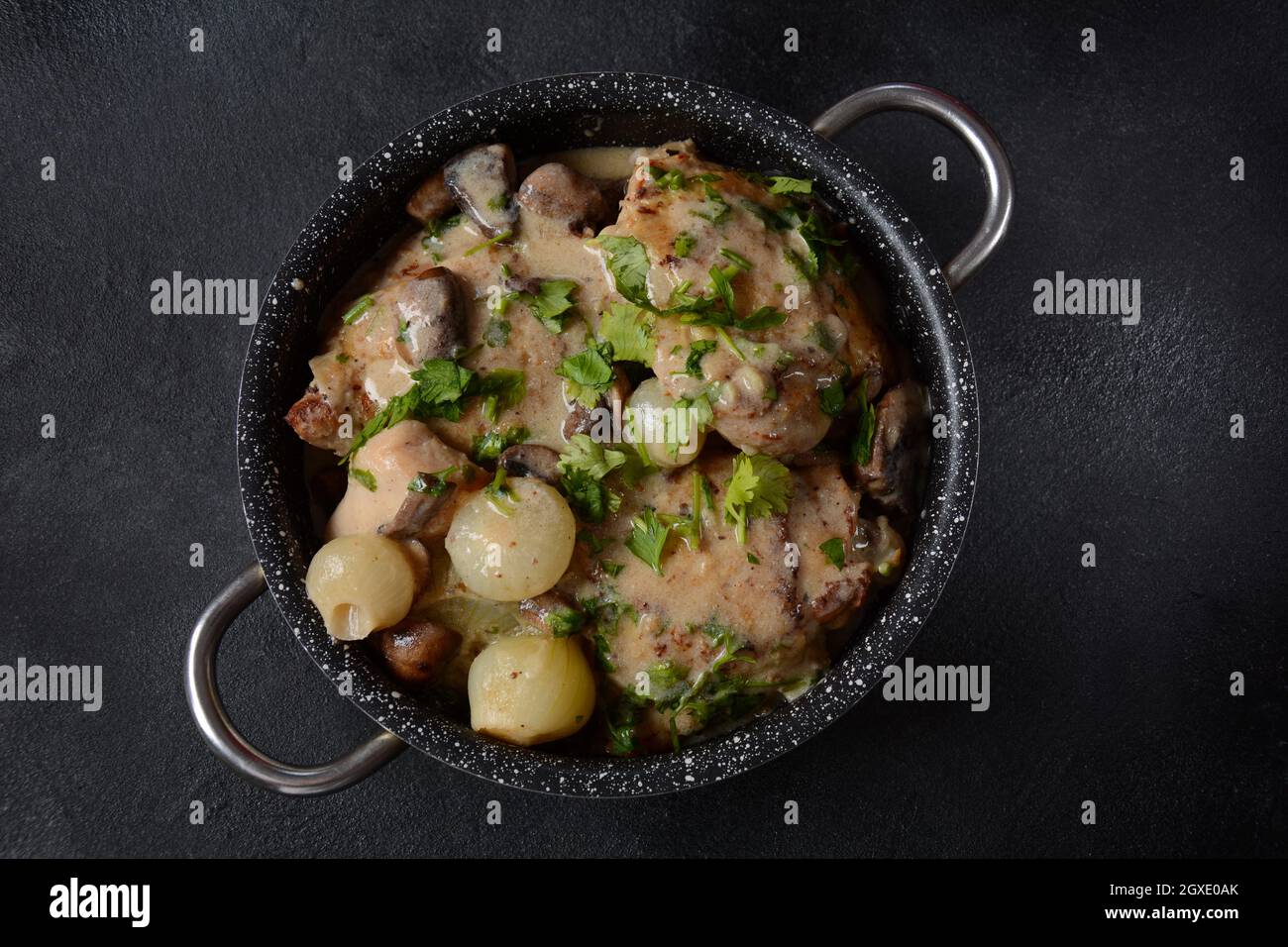 Fricassee - cuisine française. Poulet cuit dans une sauce crémeuse avec des champignons dans une casserole sur une table noire Banque D'Images