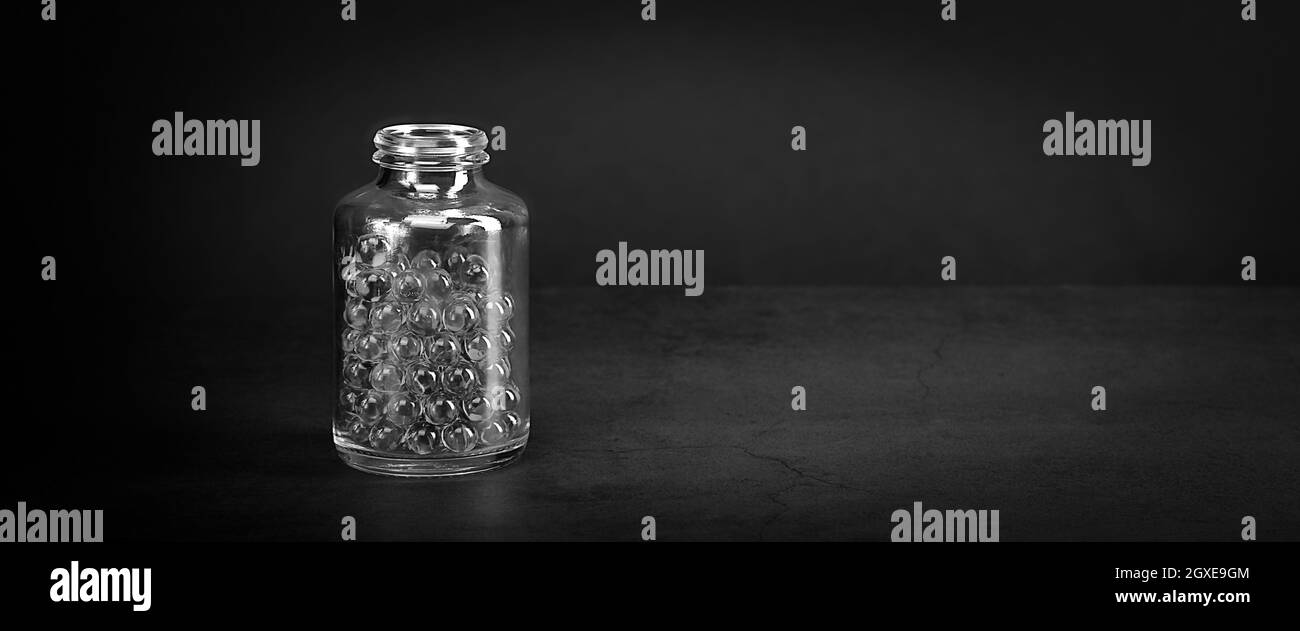 Un pot en verre avec des pilules sur fond gris. Style noir et blanc. Espace pour le lettrage, le logo, la mise en page. Banque D'Images