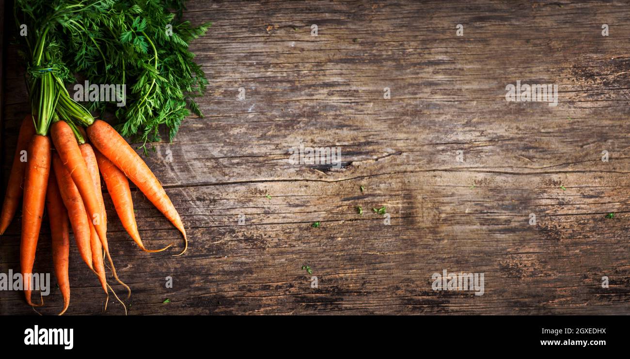 Vue de dessus des racines de carottes fraîches bio sur une table de cuisine texturée en bois. Bandeau de fond de cuisine avec espace publicitaire Banque D'Images