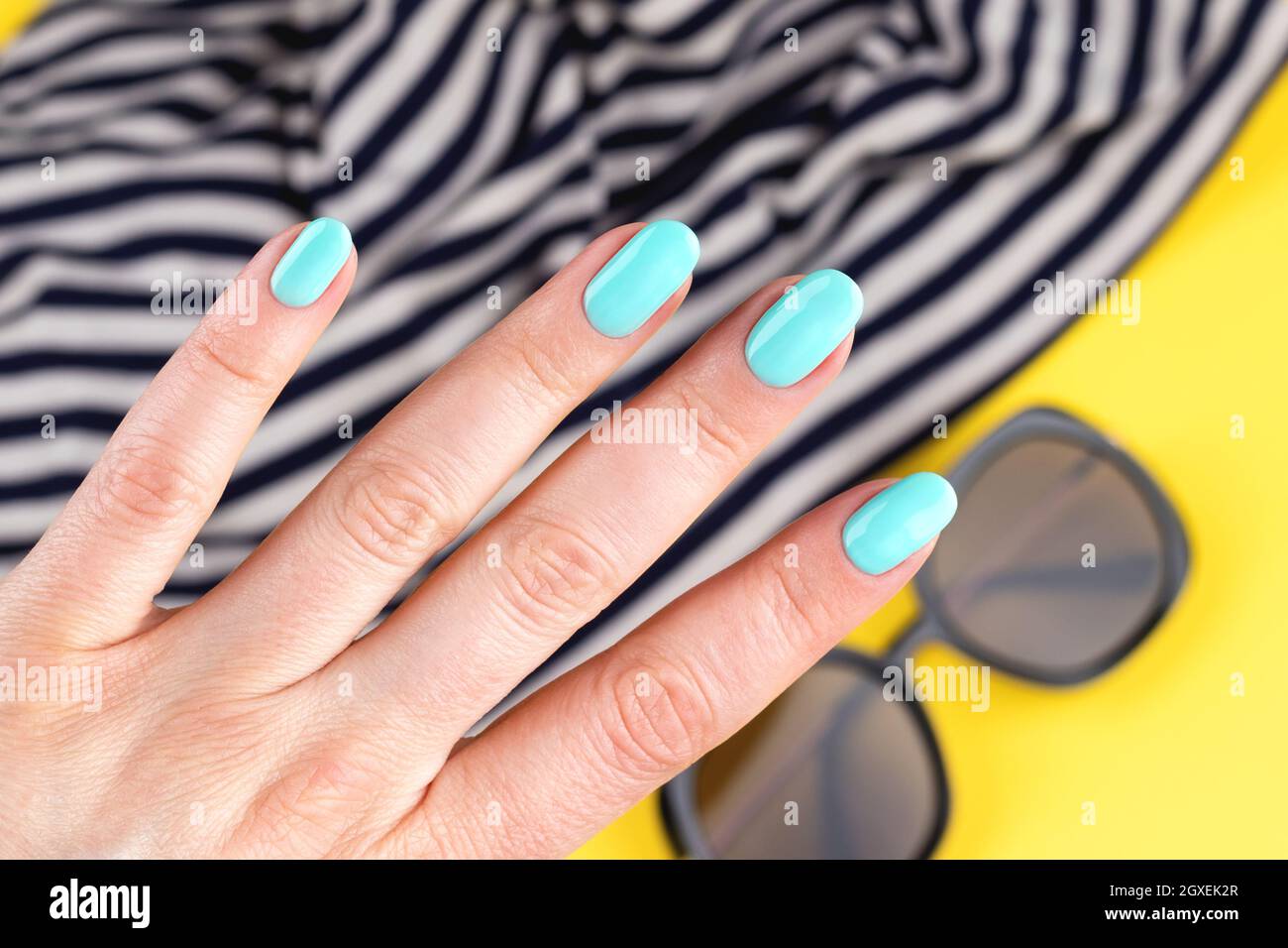 Main féminine avec belle manucure - turquoise, ongles bleu menthe sur fond  jaune avec lunettes de soleil et voile tissu rayé, gros plan, sélectif FO  Photo Stock - Alamy