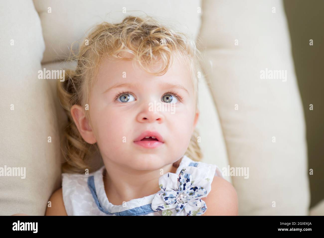 Adorable blonde aux yeux bleus et aux cheveux Petite fille assise dans la chaise. Banque D'Images