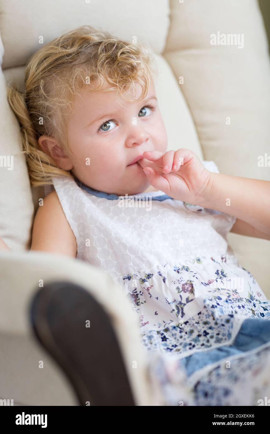 Adorable blonde aux yeux bleus et aux cheveux Petite fille assise dans la chaise. Banque D'Images