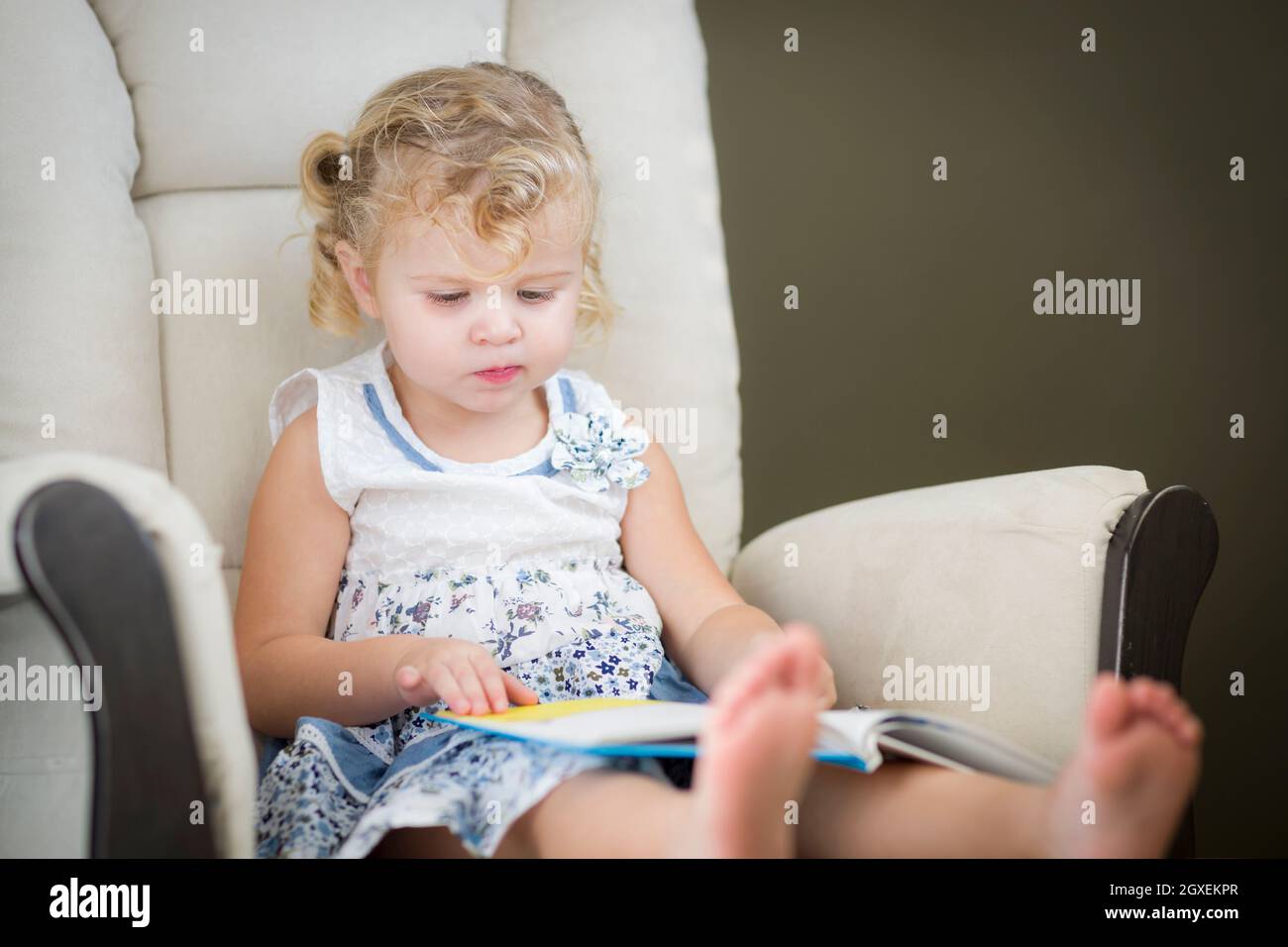 Blond aux yeux bleu adorable petite fille lisant son livre dans la présidence. Banque D'Images