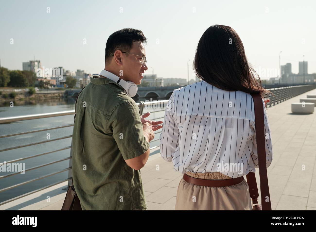 Vue arrière de deux jeunes collègues chinois se promenant le long de la rivière et interagissant Banque D'Images