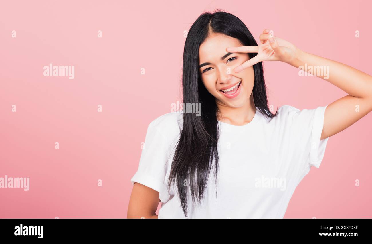 Asiatique heureux portrait beau mignon jeune femme adolescent sourire debout montrant le symbole de victoire du signe en v du doigt à côté de l'œil prise de vue en studio Banque D'Images