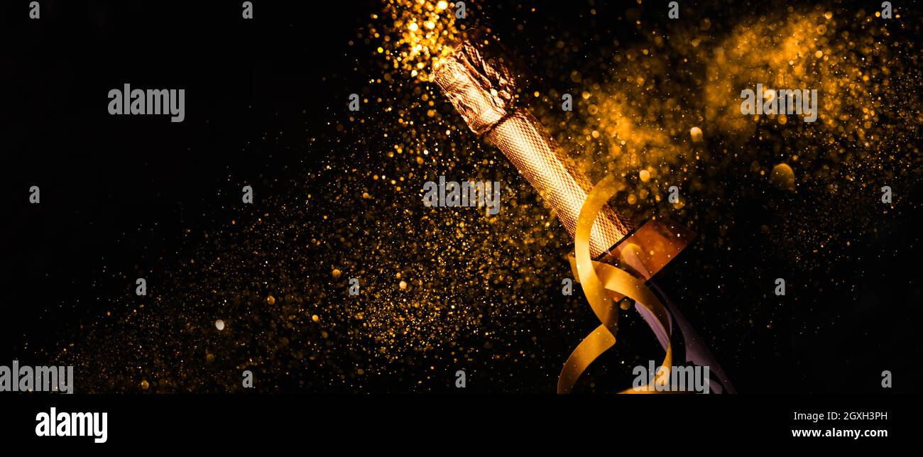 Expérience du nouvel an de luxe. Bouteille de champagne avec ruban doré sur fond sombre et feu d'artifice doré à paillettes de bokeh. Célébration de Noël panoramique d Banque D'Images