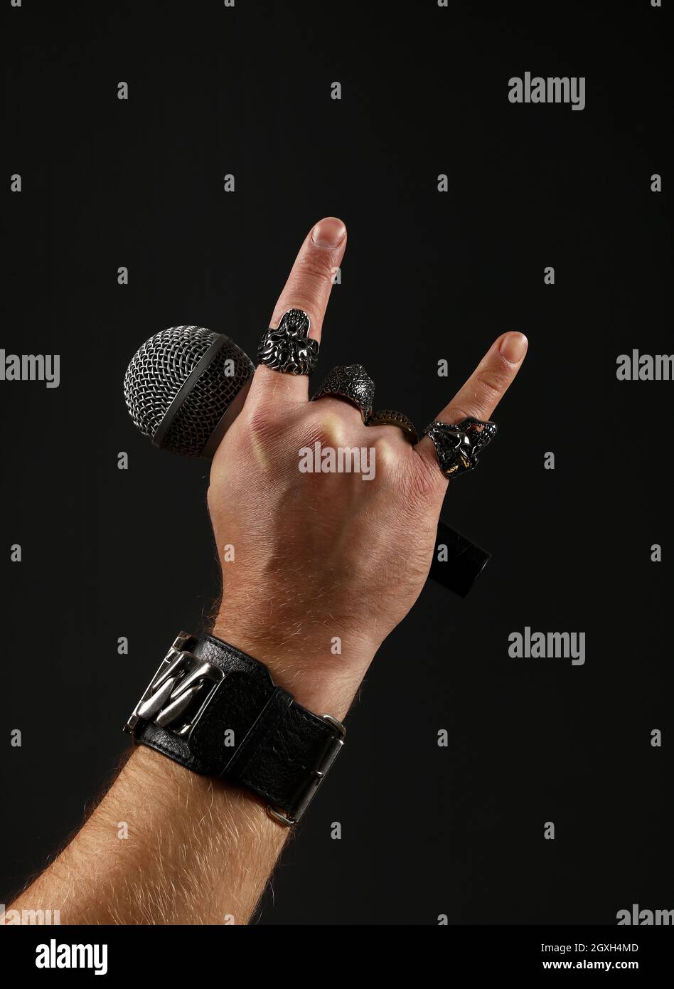 Close up man main avec anneaux en métal et bracelet montrant devil horns geste rock signe, holding microphone sur fond noir, side view Banque D'Images