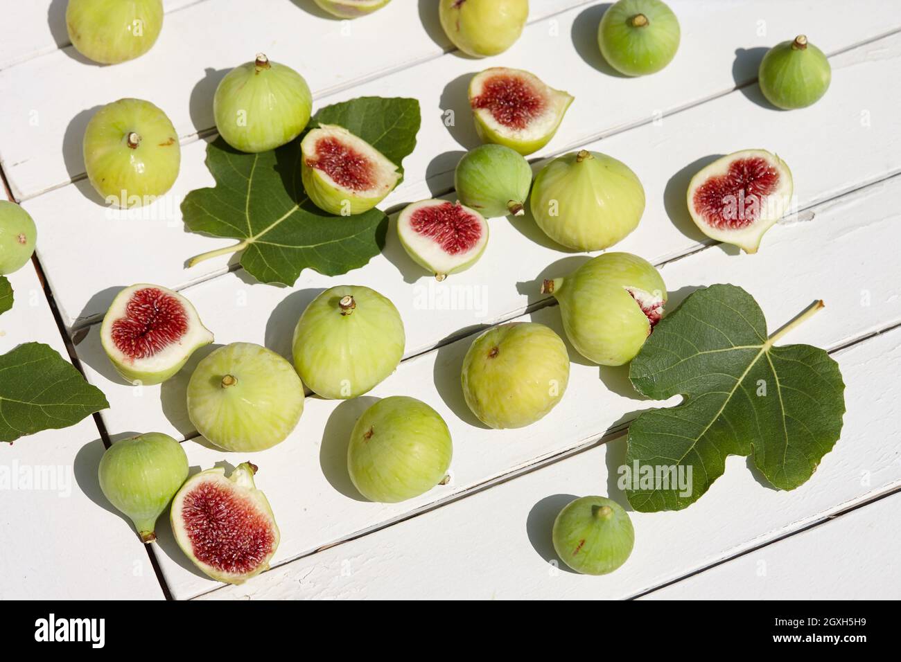 Figues vertes fraîches avec feuilles sur table en bois blanc Banque D'Images