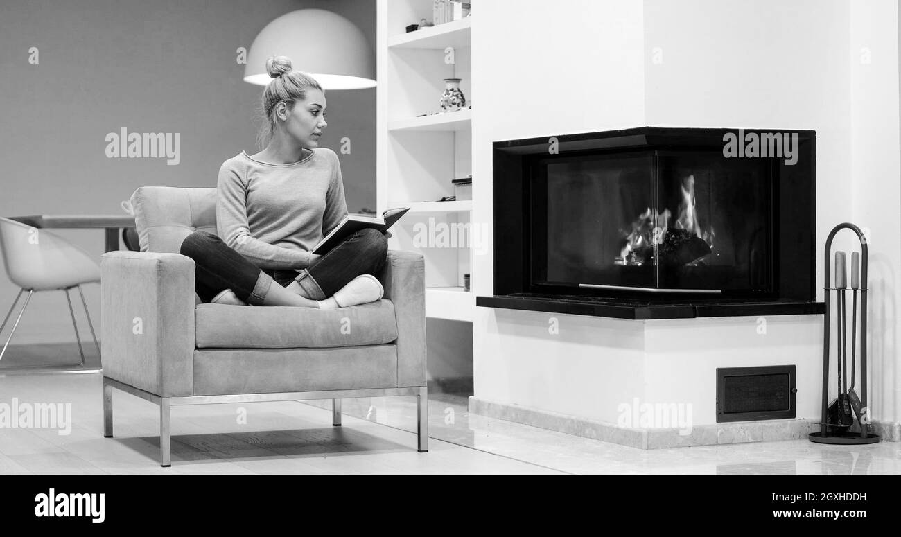 Belle Jeune femme assise en face d'une cheminée à la maison par une froide journée d'automne et reading book Banque D'Images