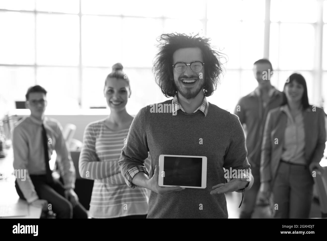 Portrait of a young businessman holding tablet in bright office avec des collègues dans l'arrière-plan Banque D'Images