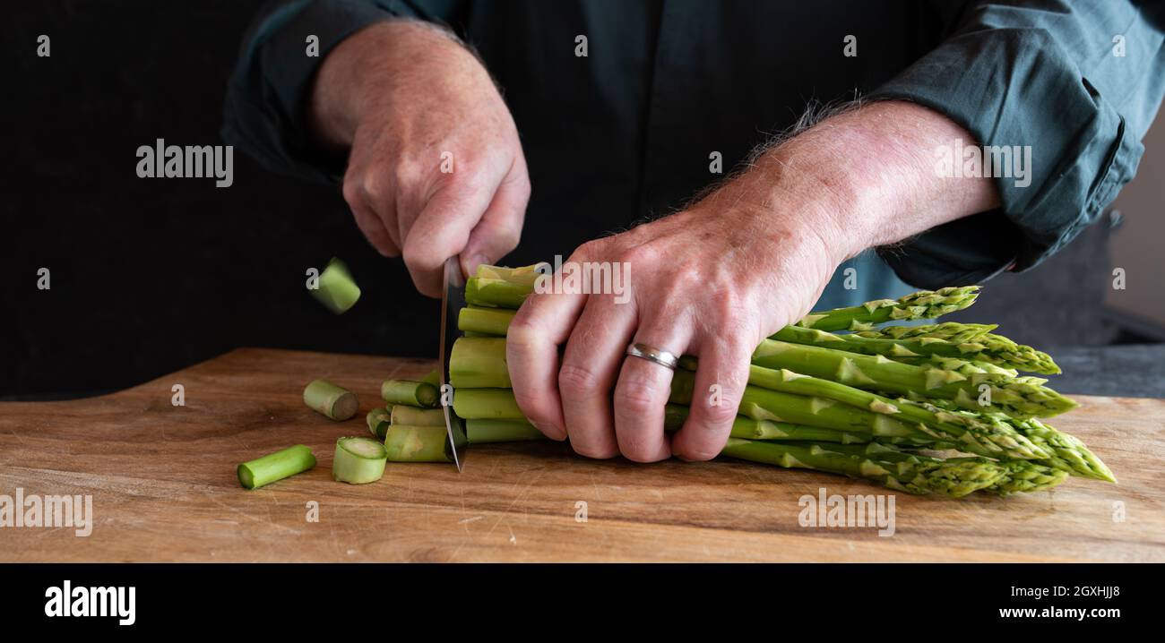 Les mains coupent des asperges vertes sur une planche à découper en bois. Légumes pour une alimentation saine concept. Gastronomie et style de vie. Gros plan. Banque D'Images