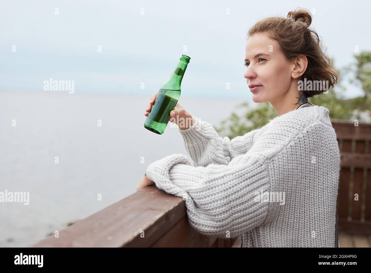 Petit portrait de la vue latérale de la jeune femme appréciant la vue sur la mer à boire de la bière à la plage, espace de copie Banque D'Images