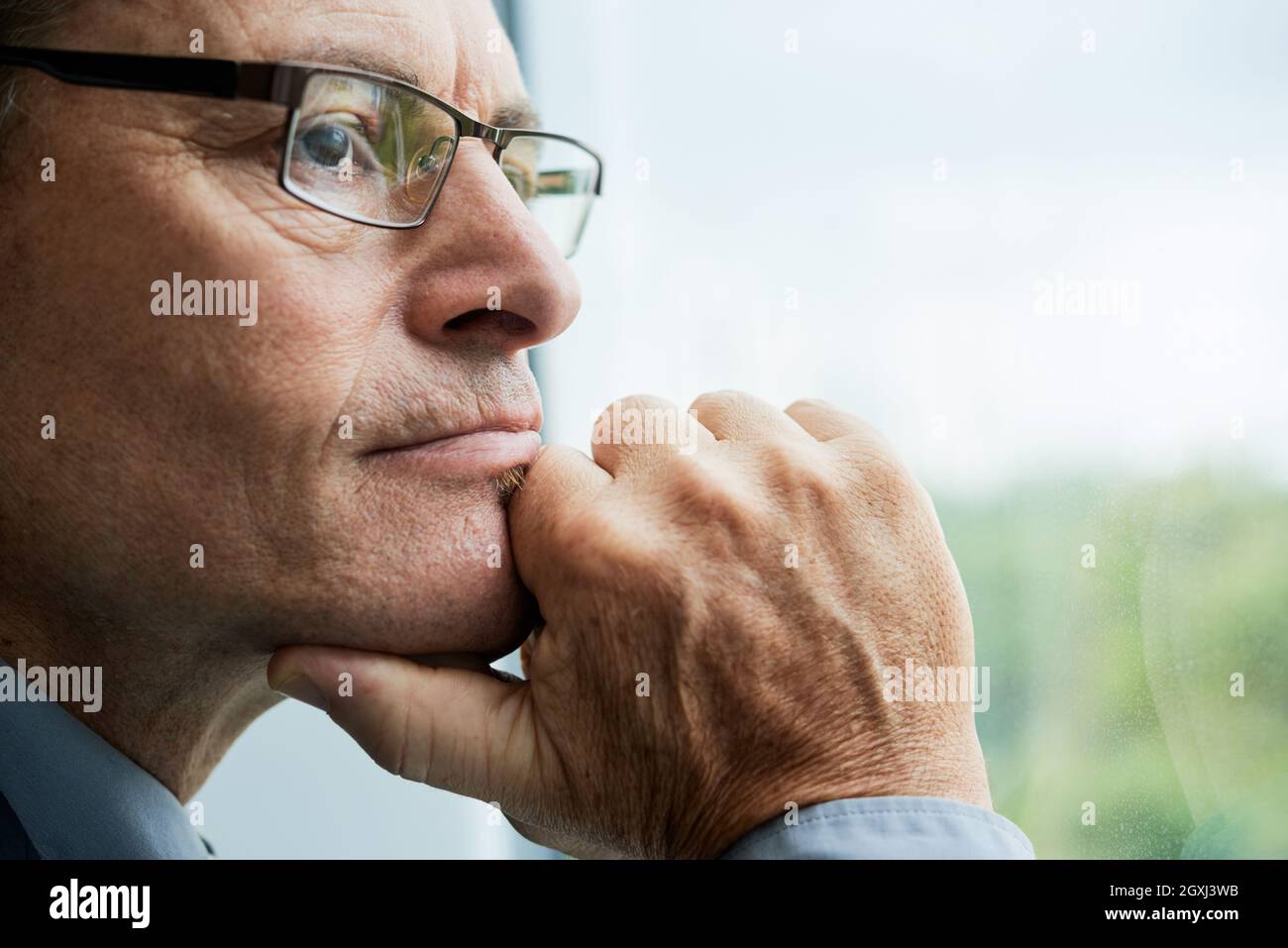 Tête de vue d'un homme caucasien mûr et réfléchi dans des lunettes touchant le menton et contemplant le paysage urbain à travers la fenêtre Banque D'Images