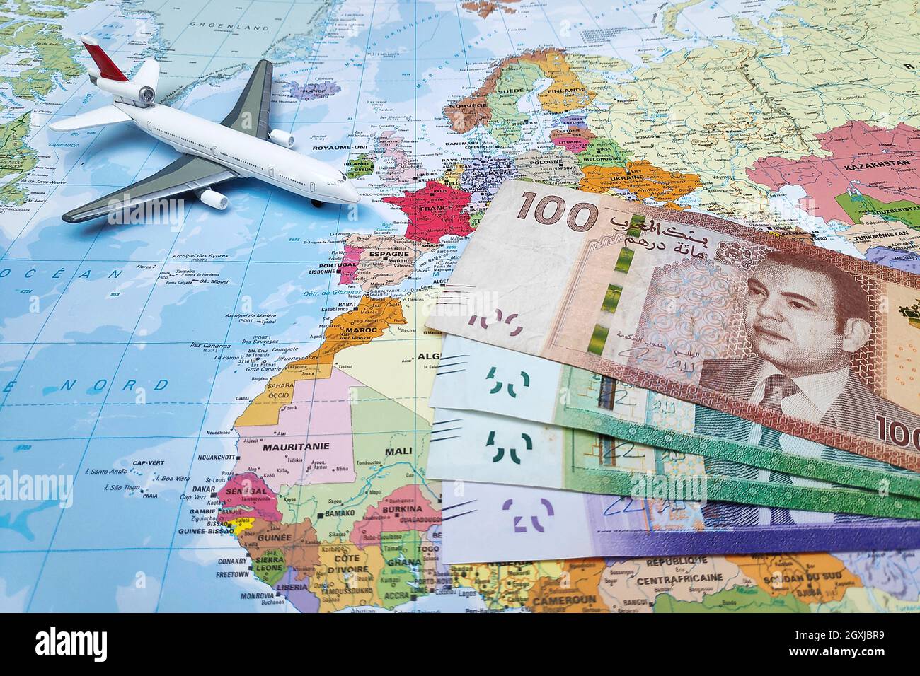 Composition composée d'une carte du monde centrée sur le Maroc avec sur elle, quelques billets de Dirham marocains ainsi qu'un avion de jouet Banque D'Images