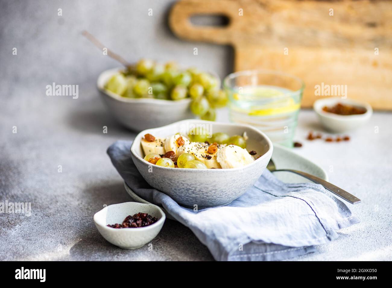 Vue panoramique sur une tasse de café, un verre d'eau de citron et un bol de porridge avec des bananes fraîches, des raisins, des baies de goji, des graines de chia et des raisins secs Banque D'Images