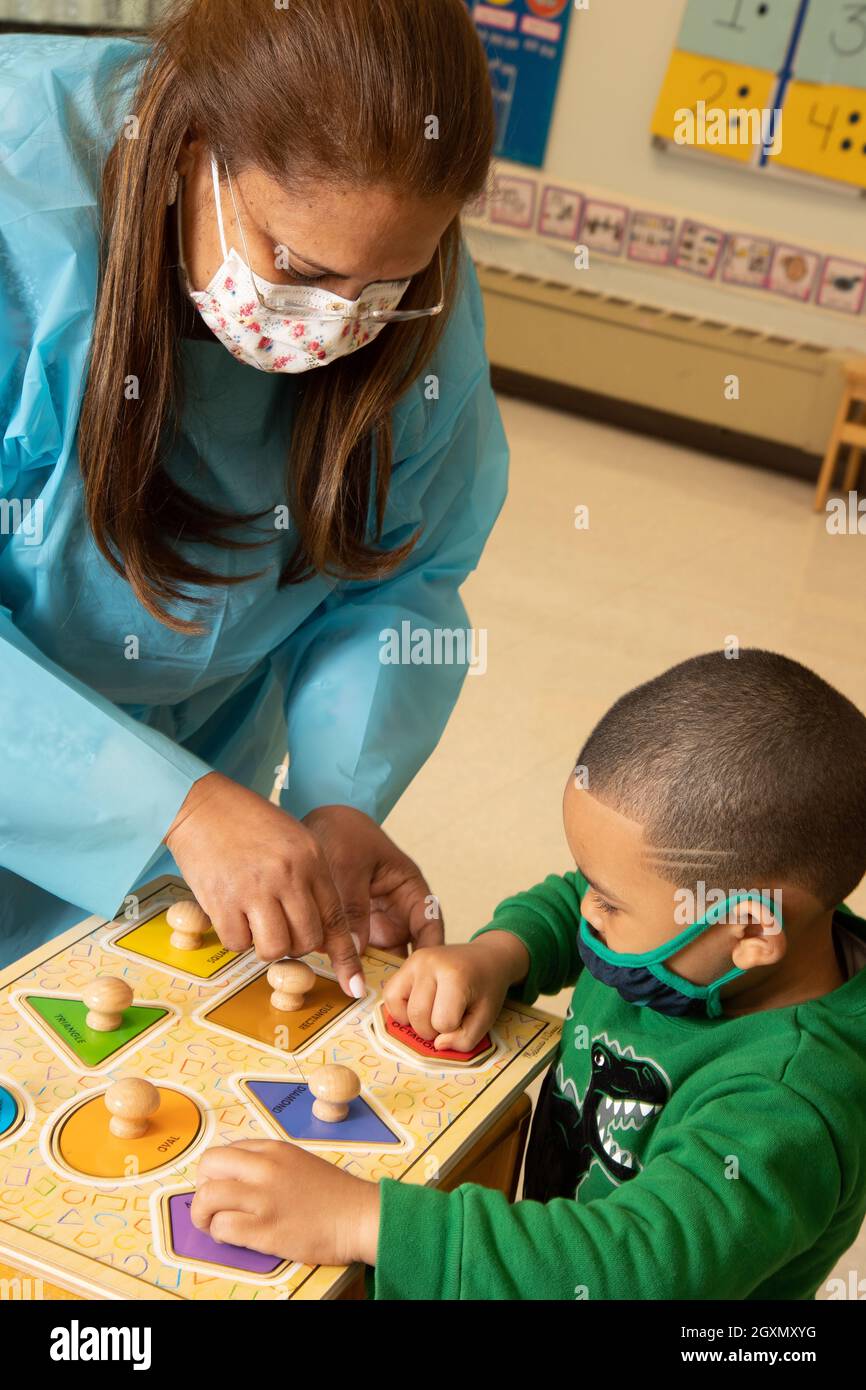 Éducation préscolaire 3-4 ans enseignante travaillant en classe avec un garçon jouant avec des formes géométriques puzzle, masques de visage à protéger contre Covid-19 Banque D'Images