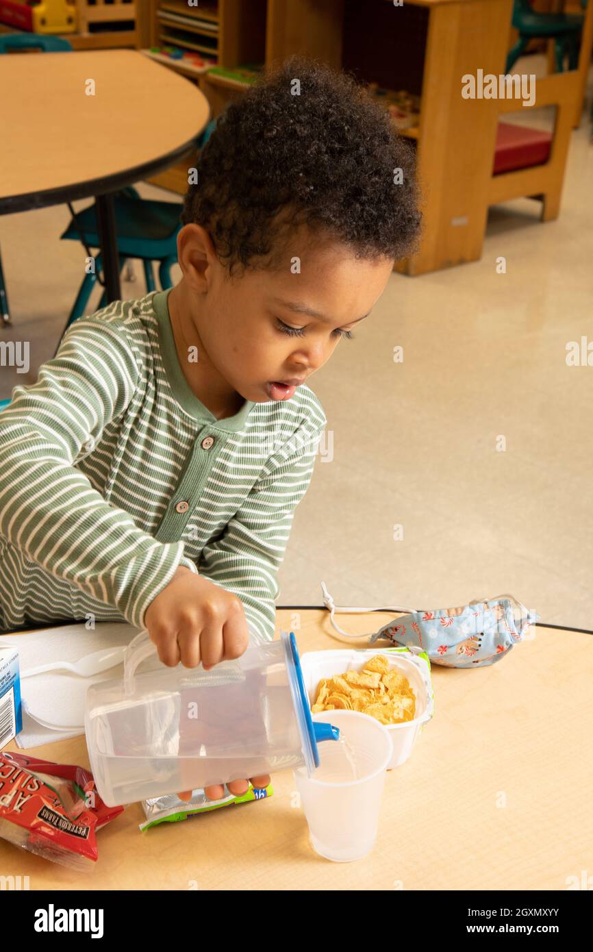 Éducation préscolaire garçon de 3-4 ans versant de l'eau dans sa tasse au petit déjeuner Banque D'Images