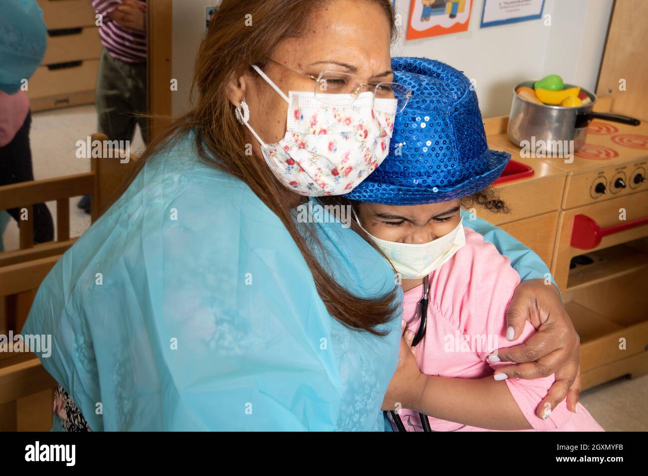 Éducation préscolaire 3-4 ans femme souriante enseignante embrassant fille porter chapeau d'habillage, tous deux portant des masques faciaux pour protéger contre Covid-19 Banque D'Images