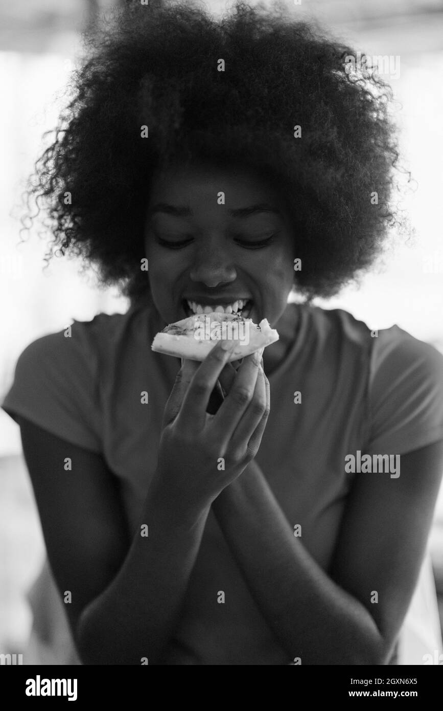 Très jeune hangry african american woman with afro hairstyle eating pizza savoureuse tranche dans fast food restaurant Banque D'Images