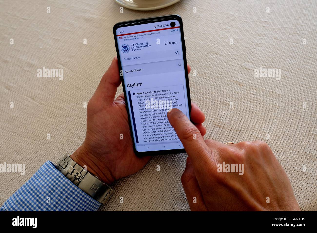 Homme sur le site Web des services de citoyenneté et d'immigration des États-Unis sur un téléphone portable lisant les règles et les règlements régissant les demandeurs d'asile aux États-Unis. Banque D'Images