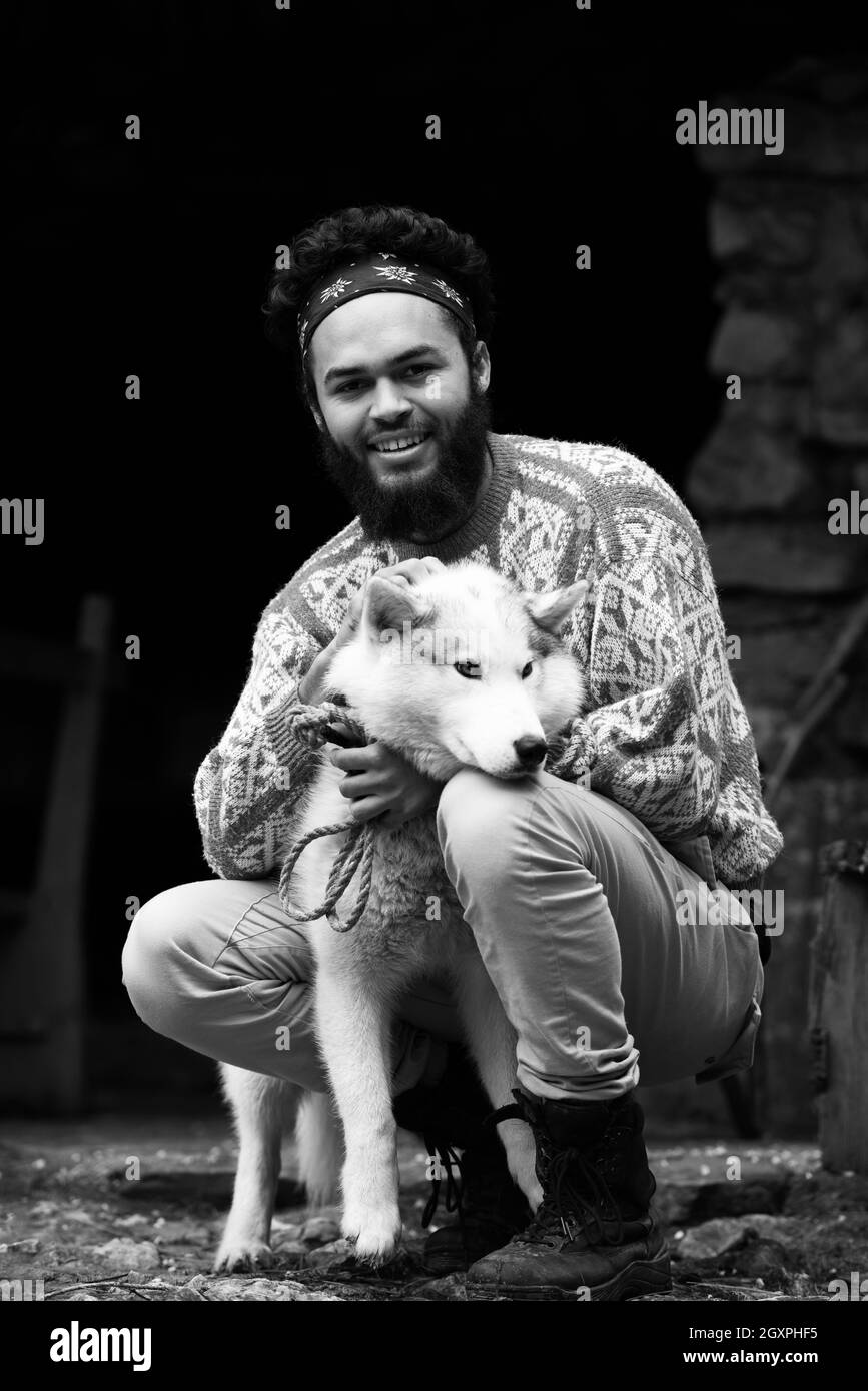 Hipster beau jeune homme debout avec chien husky blanc en face de l'ancienne maison en bois rétro vintage Banque D'Images