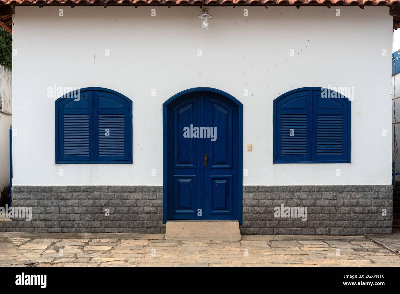 Murs blancs, porte et fenêtres bleues, vue sur la façade de la maison paroissiale Sant’Ana de Inconfidencia à Sebollas, Paraiba do Sul, Brésil.L'église et la maison Banque D'Images