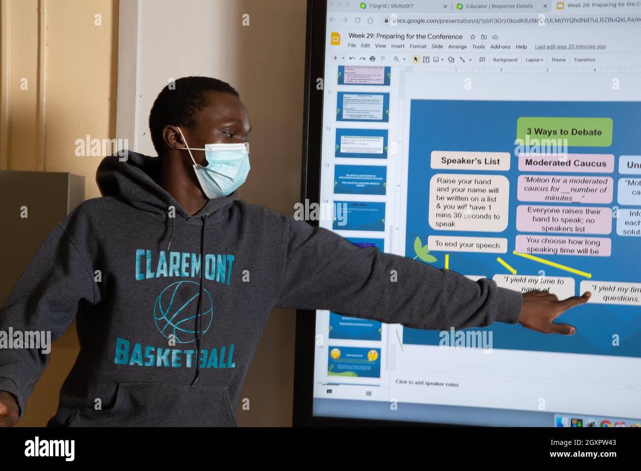 Éducation secondaire classe étudiant de sexe masculin présentant à la classe en utilisant le tableau intelligent, pointant vers la section, portant un masque pour protéger Covid-19 Banque D'Images