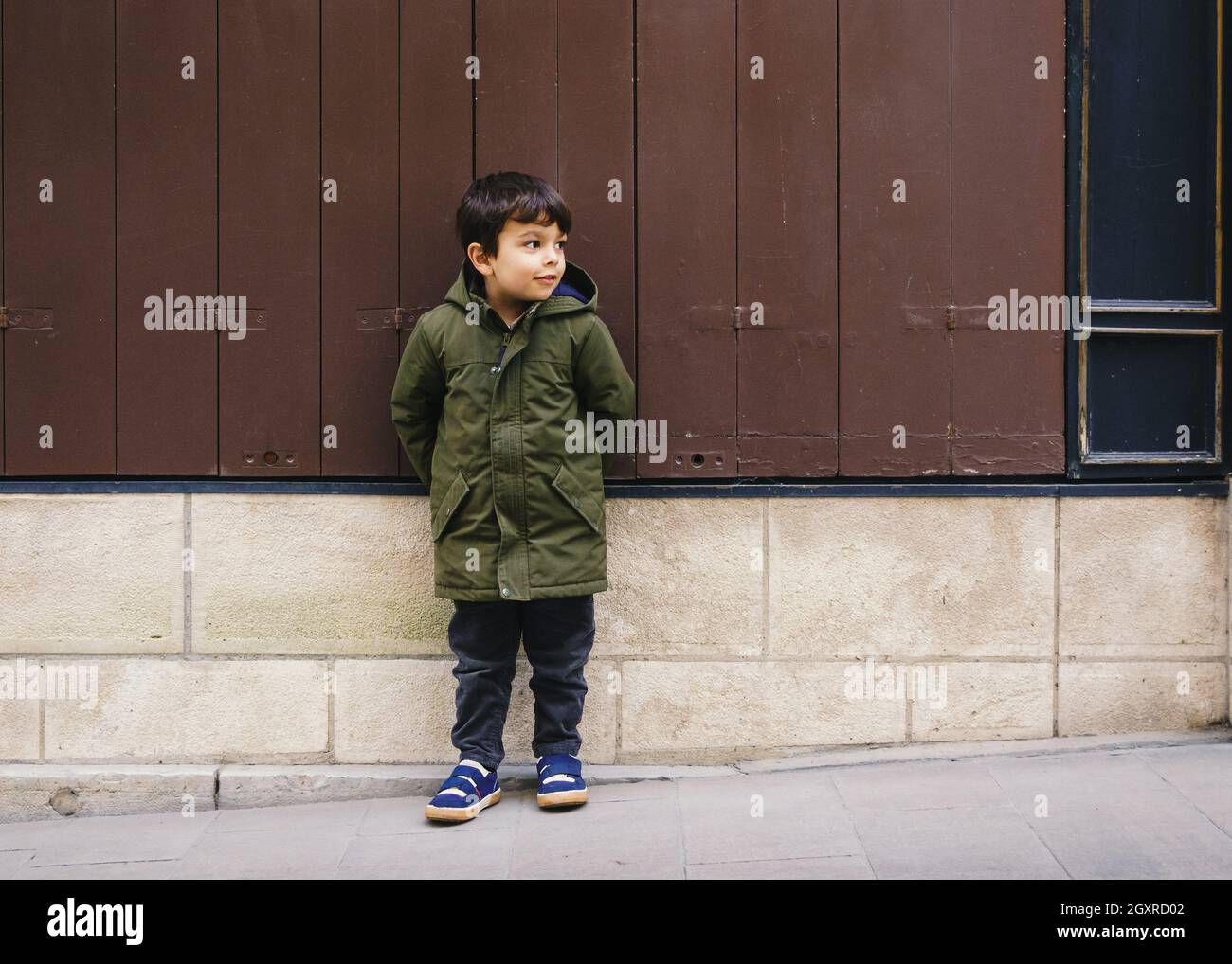 Petit garçon en manteau vert contre un mur d'aspect vintage Banque D'Images
