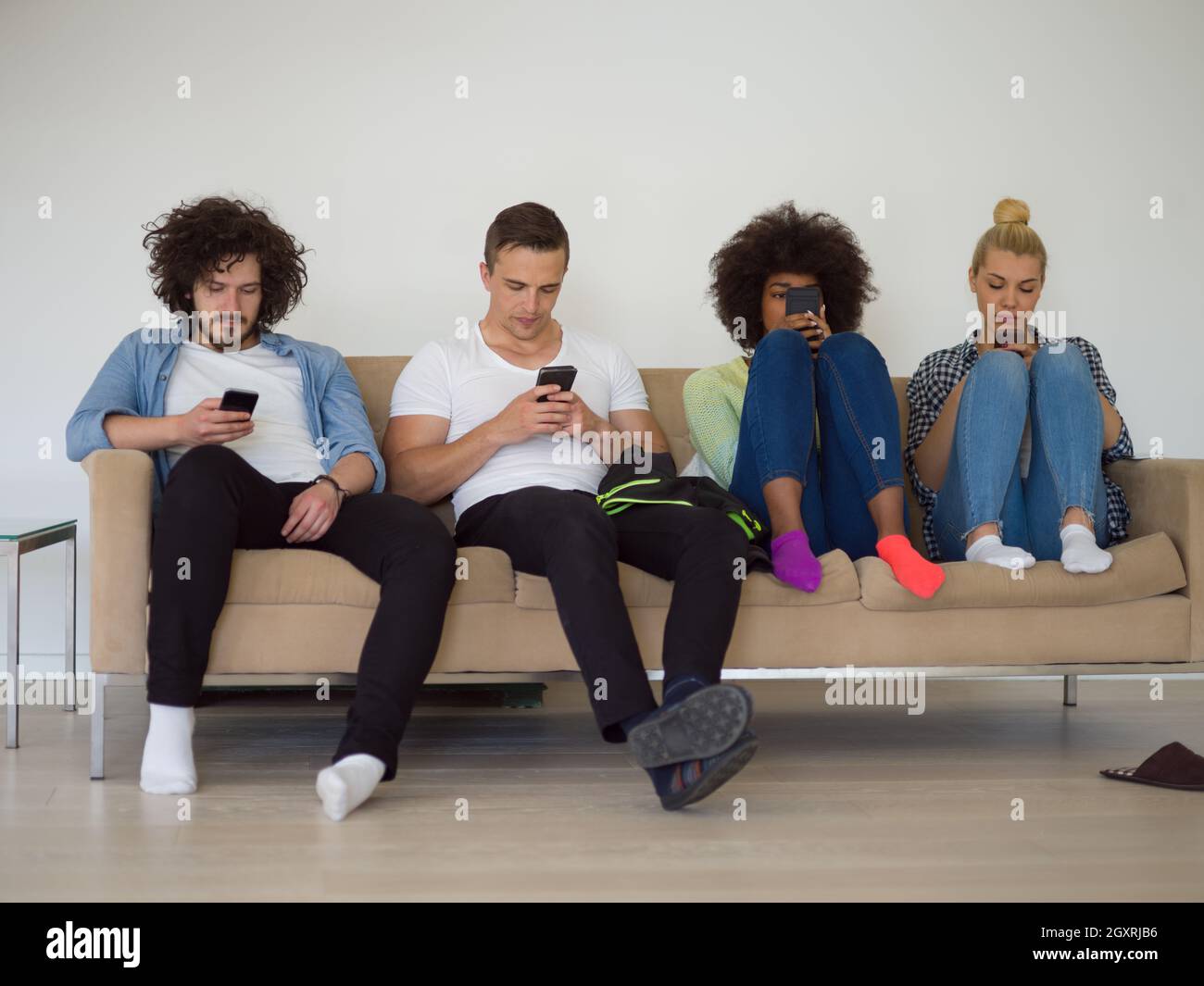 Groupe multiethnique de jeunes gens assis sur un canapé à la maison à regarder,smartphone, smartphone, antisocial en toxicomanie Banque D'Images