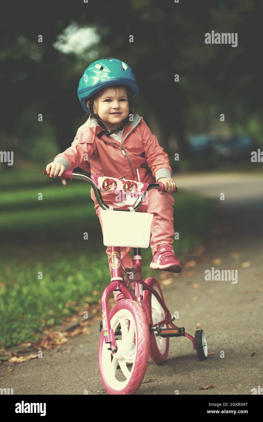 Cute smiling little girl avec Vélo et casque sur la route dans le parc Banque D'Images