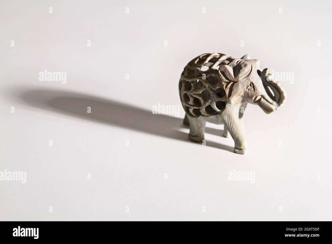 Vue de trois quarts d'un petit éléphant en pierre qui jette une longue ombre sur un fond blanc Banque D'Images