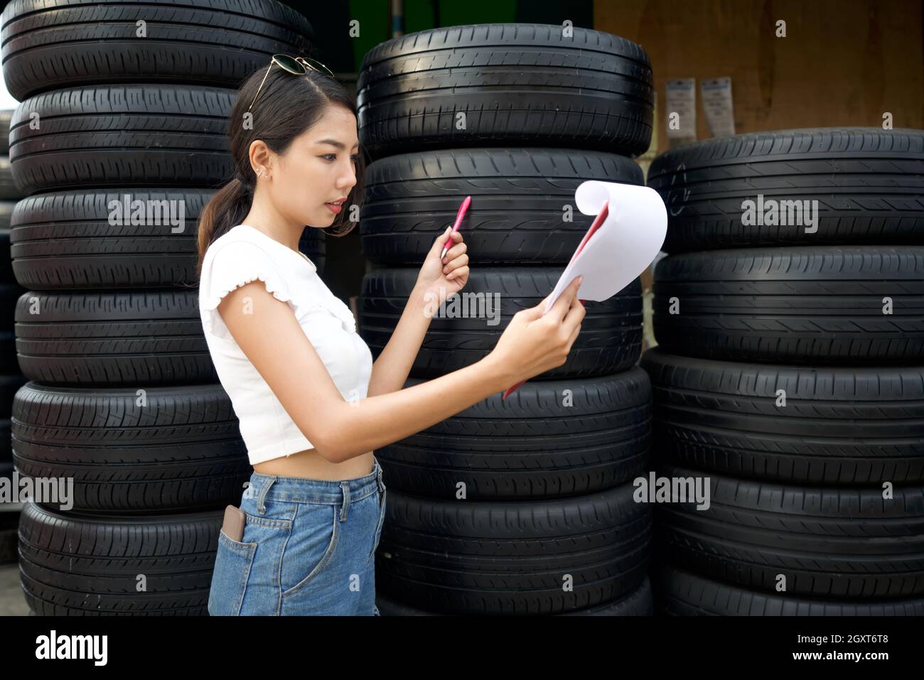Le jeune propriétaire asiatique du magasin de pièces automobiles vérifie le nombre de pneus et les commandes reçues avant de commencer le travail le matin. Plusieurs pneus de voiture sont Banque D'Images