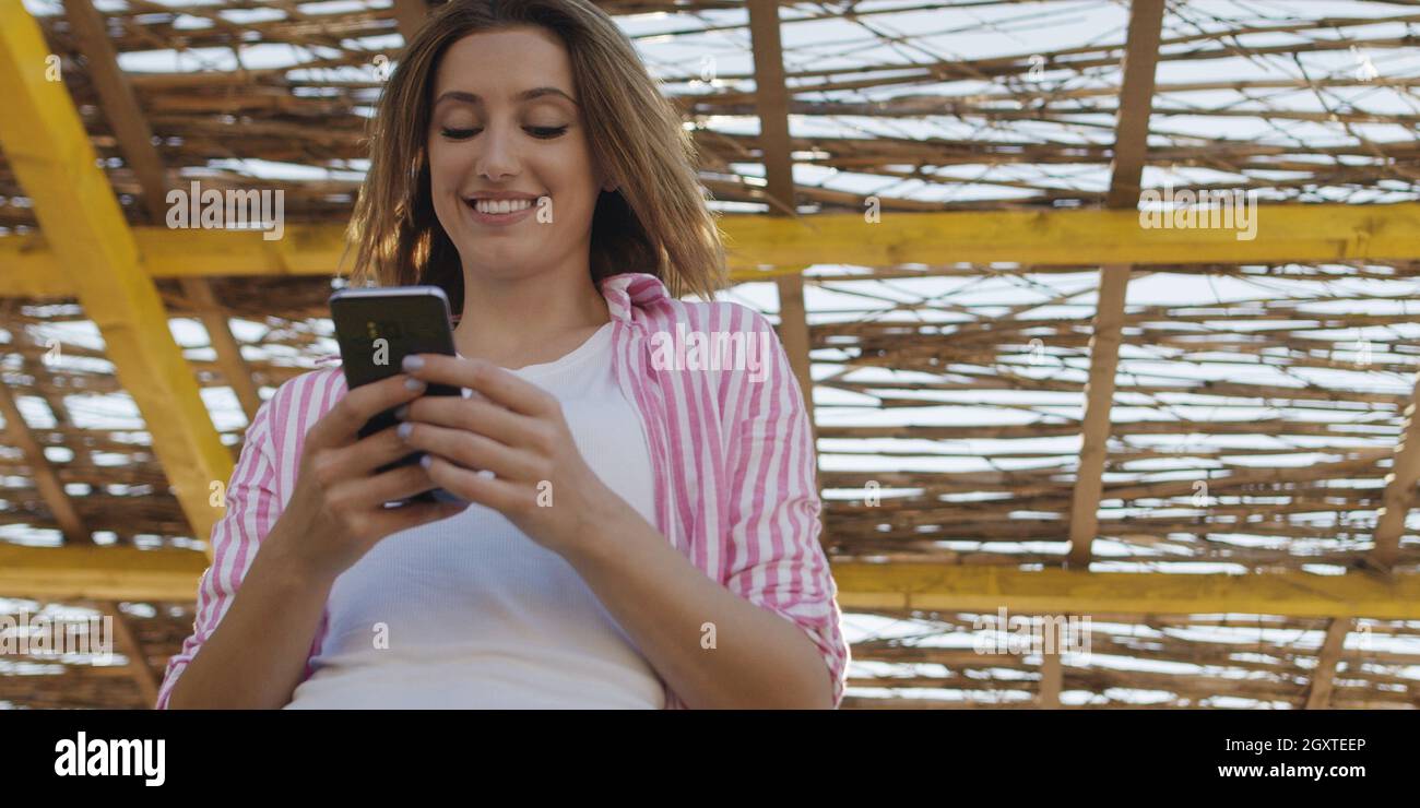 Jeune femme à l'aide de mobile cell smart phone app à la plage pendant le coucher du soleil sur la journée d'automne Banque D'Images