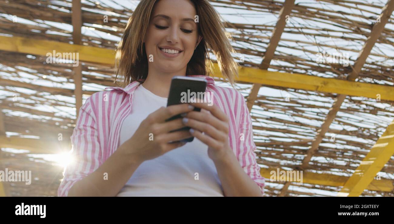 Jeune femme à l'aide de mobile cell smart phone app à la plage pendant le coucher du soleil sur la journée d'automne Banque D'Images