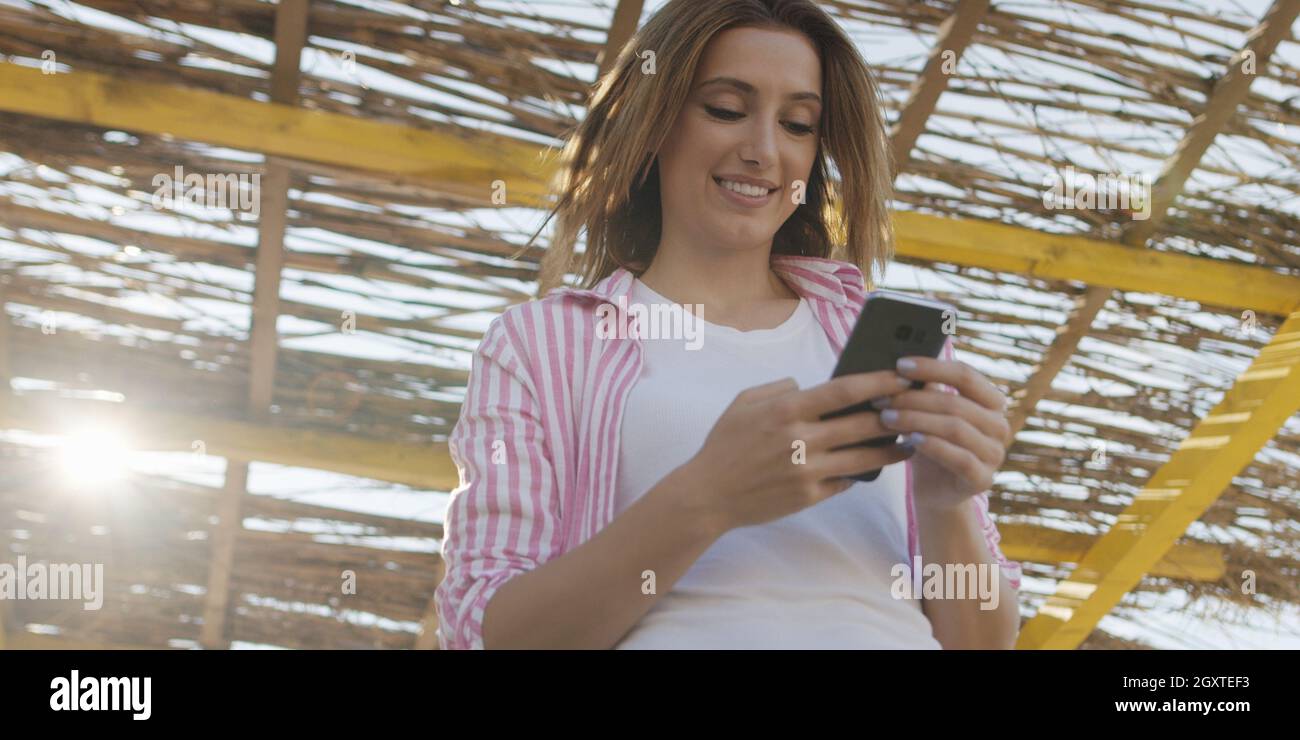 Jeune femme à l'aide de mobile cell smart phone app à la plage pendant le coucher du soleil sur la journée d'automne Banque D'Images