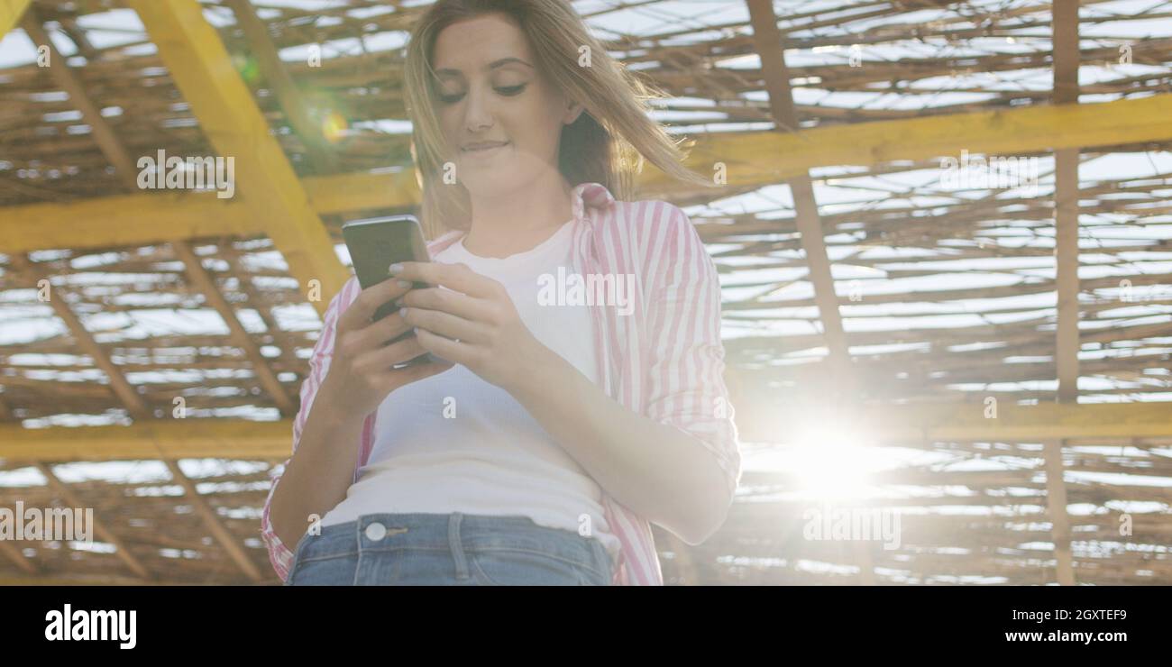 Jeune femme à l'aide de mobile cell smart phone app à la plage pendant le coucher du soleil sur la journée d'automne Banque D'Images