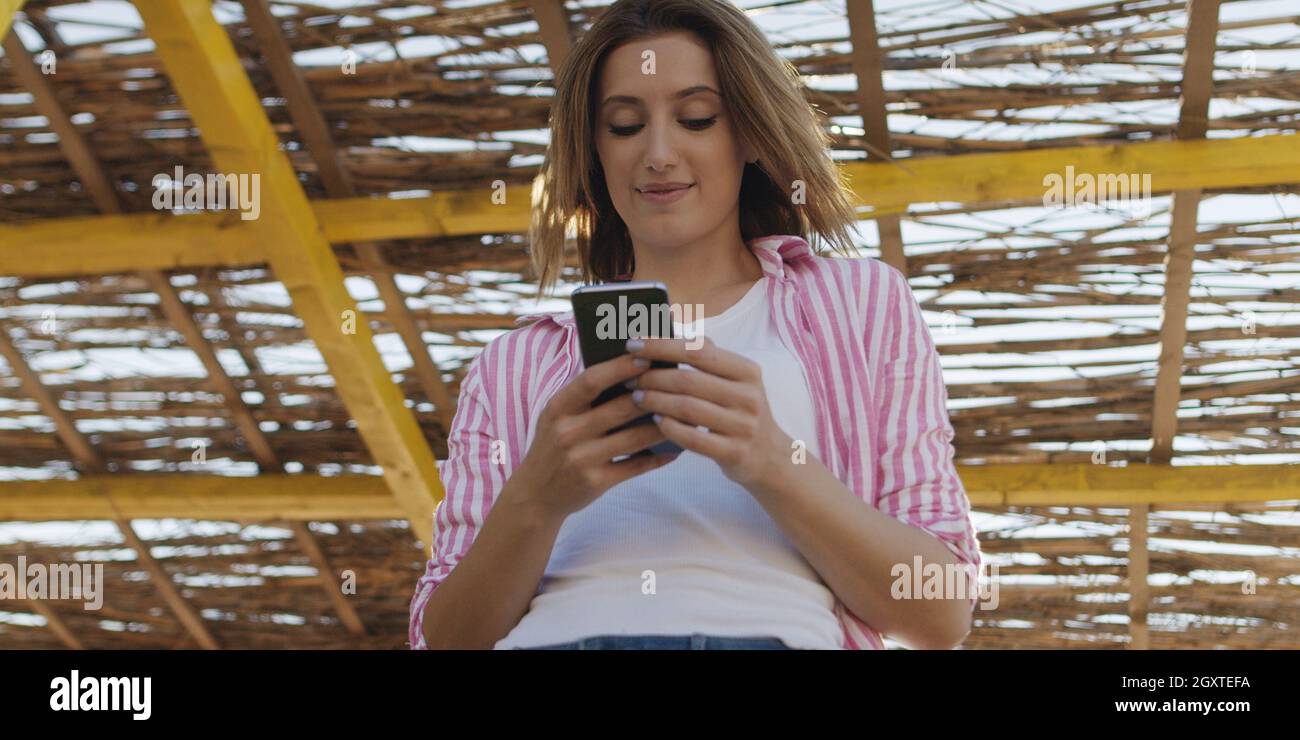 Jeune femme à l'aide de mobile cell smart phone app à la plage pendant le coucher du soleil sur la journée d'automne Banque D'Images