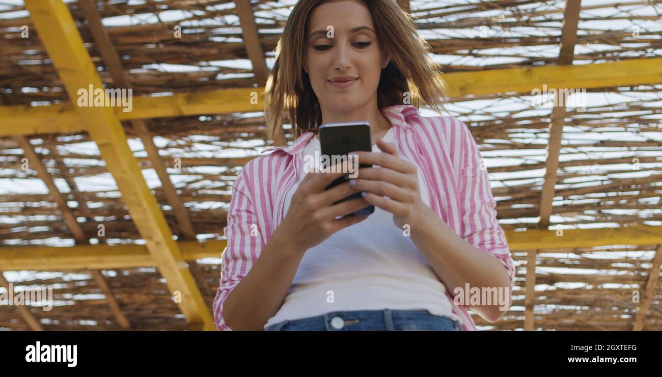 Jeune femme à l'aide de mobile cell smart phone app à la plage pendant le coucher du soleil sur la journée d'automne Banque D'Images