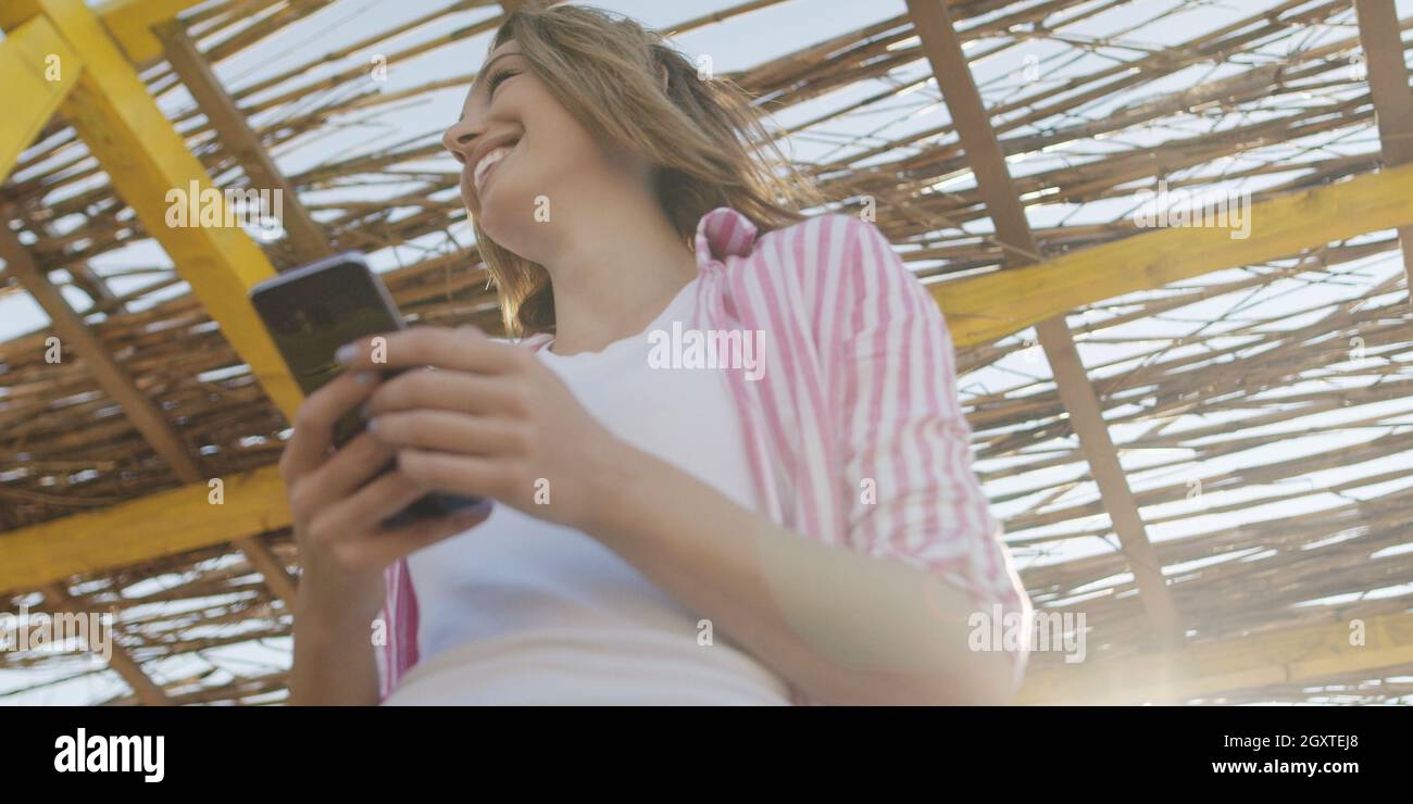 Jeune femme à l'aide de mobile cell smart phone app à la plage pendant le coucher du soleil sur la journée d'automne Banque D'Images