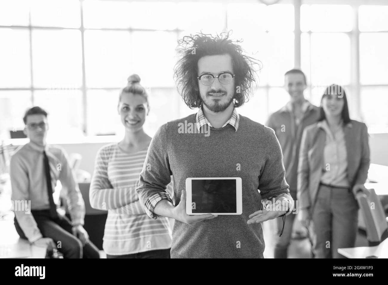 Portrait of a young businessman holding tablet in bright office avec des collègues dans l'arrière-plan Banque D'Images