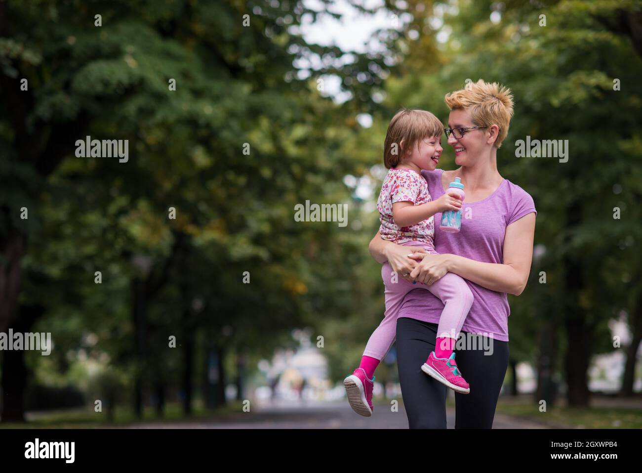 jeune mère sportive porte la petite fille dans les bras tout en faisant du jogging dans un parc de la ville, des sports de plein air et de la forme physique Banque D'Images