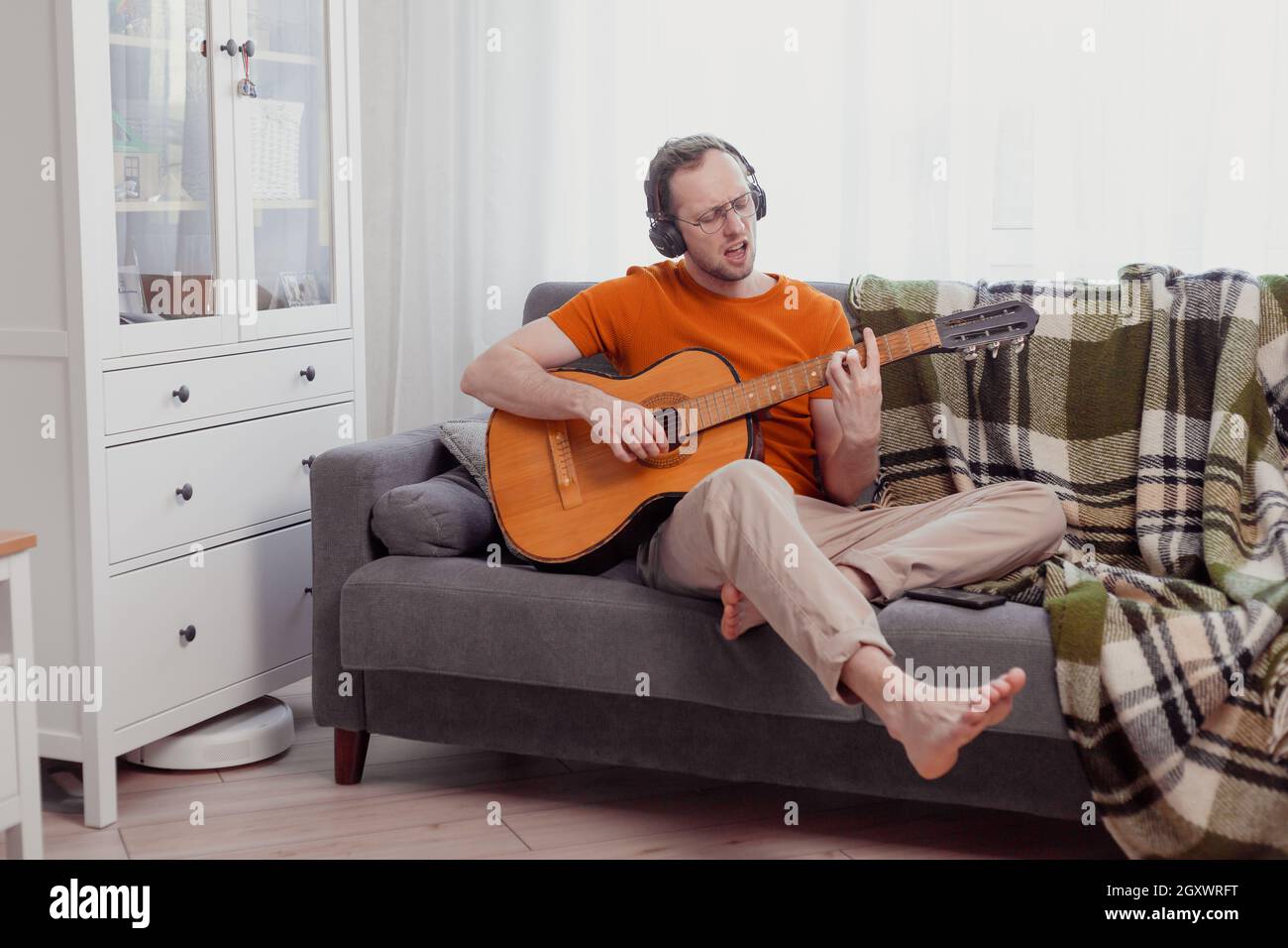 Jeune homme caucasien dans un casque jouant de la guitare et chantant à la maison. Quarantaine et hobbies concept. Pratique de la musique, photo de style de vie Banque D'Images