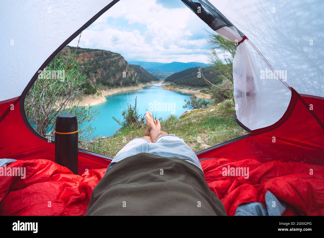 Homme couché et relaxant dans la tente dans la nature. Vue de l'intérieur de la tente sur le lac et les montagnes. Camping ou tente Banque D'Images
