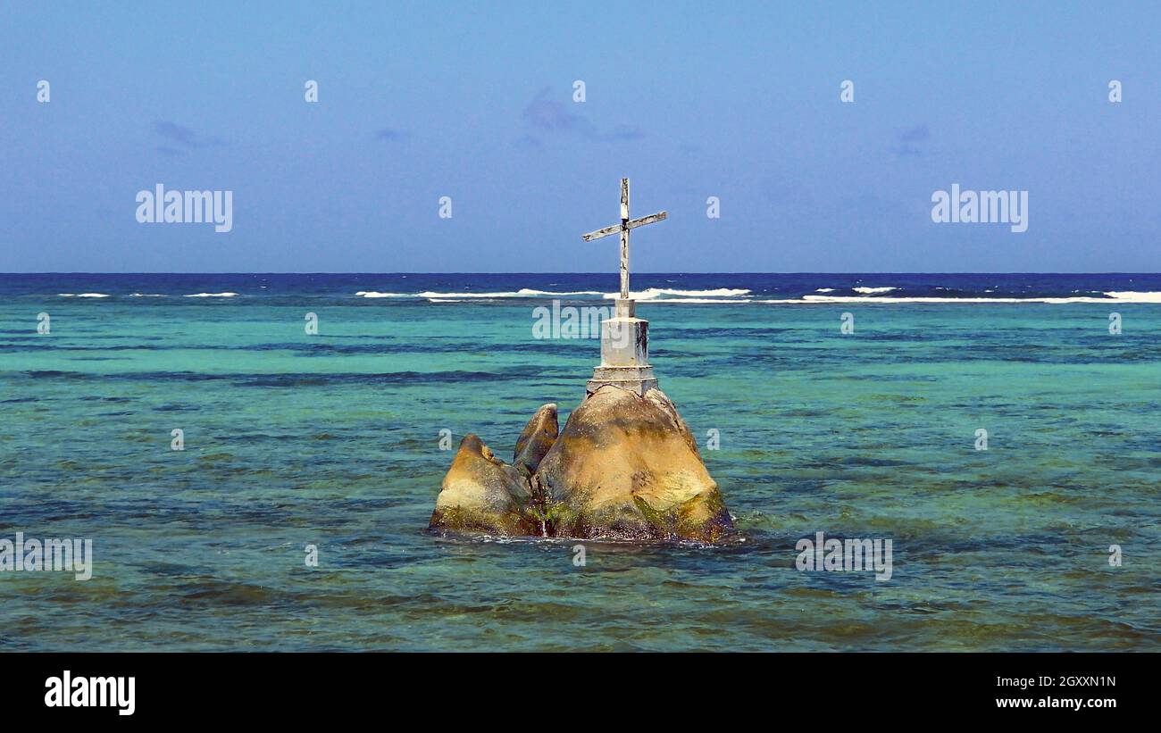 Une croix en bois patiné blanc sur les rochers dans les eaux bleu turquoise de la côte de Seychelles Banque D'Images