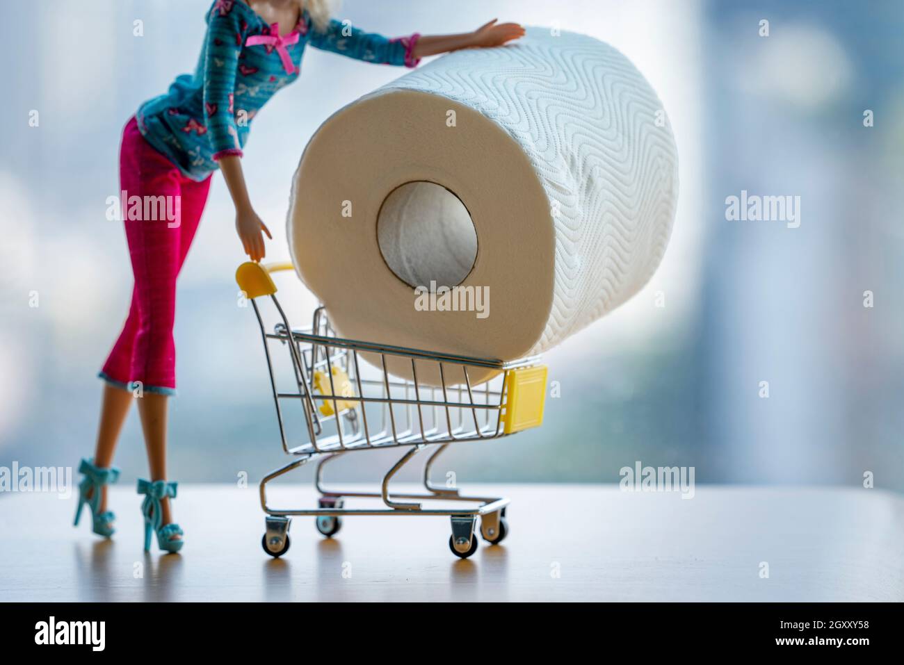 Poupée fabriquée femme poussant chariot chariot chariot d'atelier rempli de papier toilette géant sur fond clair.Mode fille achat panique shopping coron Banque D'Images