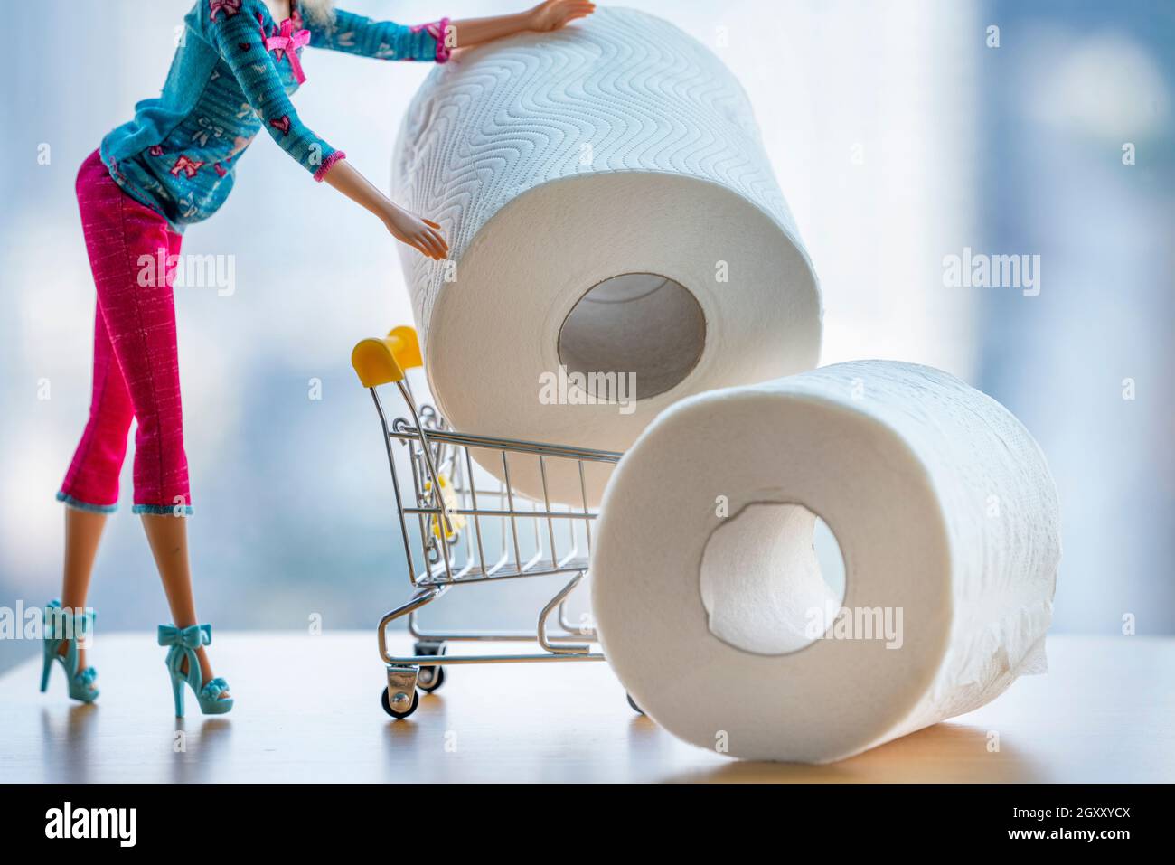 Poupée fabriquée femme poussant chariot chariot chariot d'atelier rempli de papier toilette géant sur fond clair.Mode fille achat panique shopping coron Banque D'Images