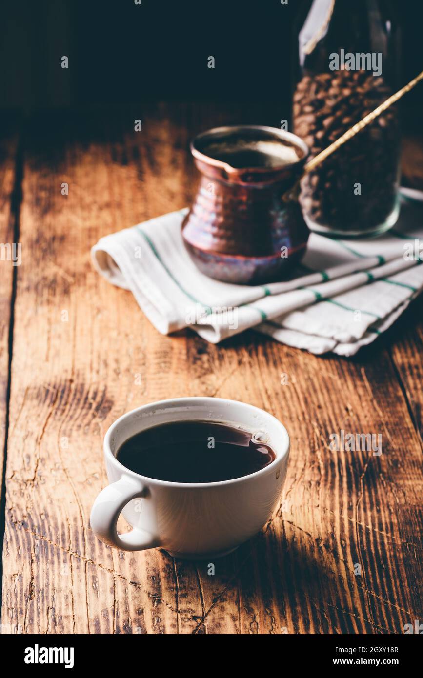 Une tasse de café turc avec de la cève de cuivre et un pot de grains de café torréfiés sur une table en bois Banque D'Images