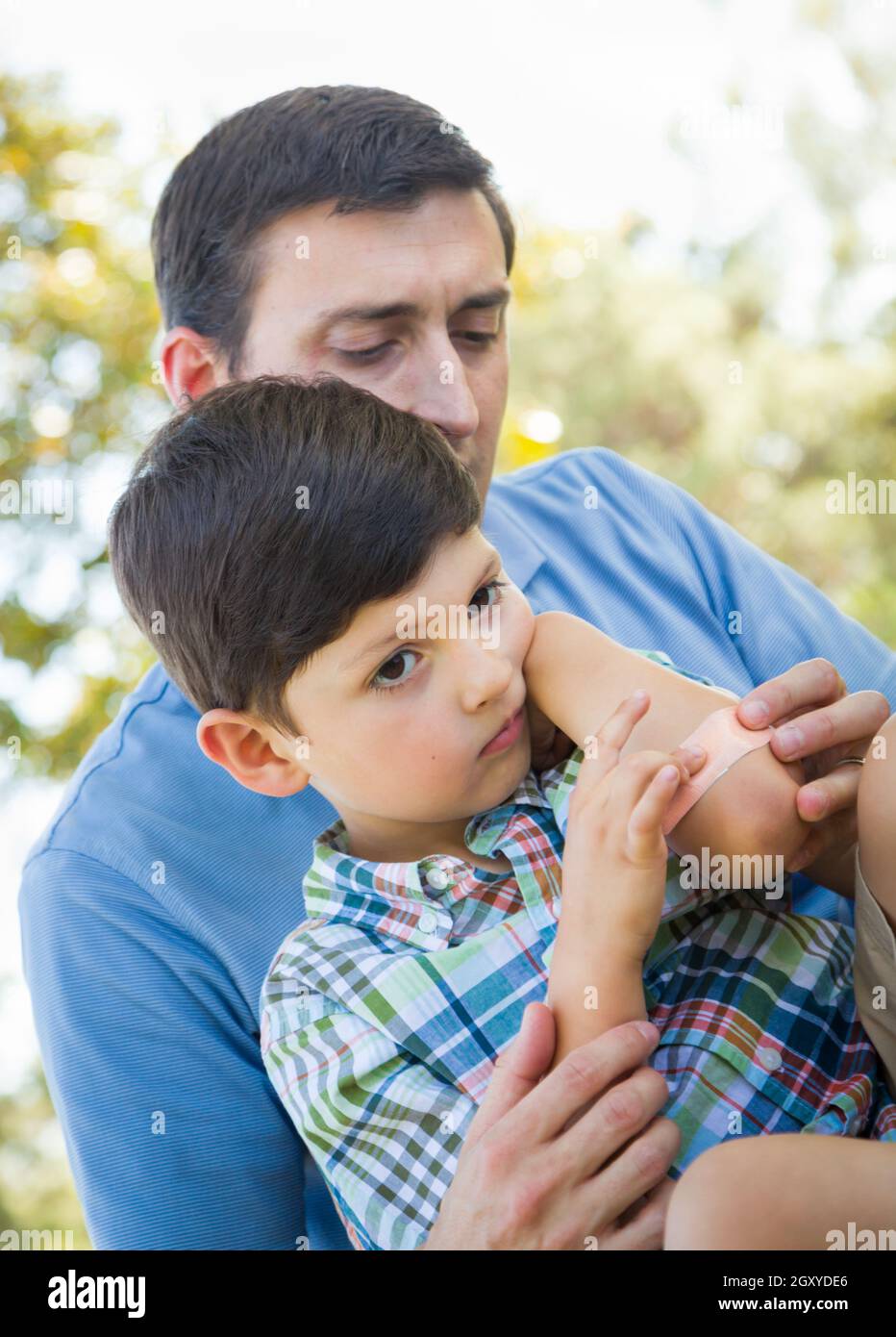 Père aimant met un bandage sur le coude de son jeune fils dans le parc. Banque D'Images