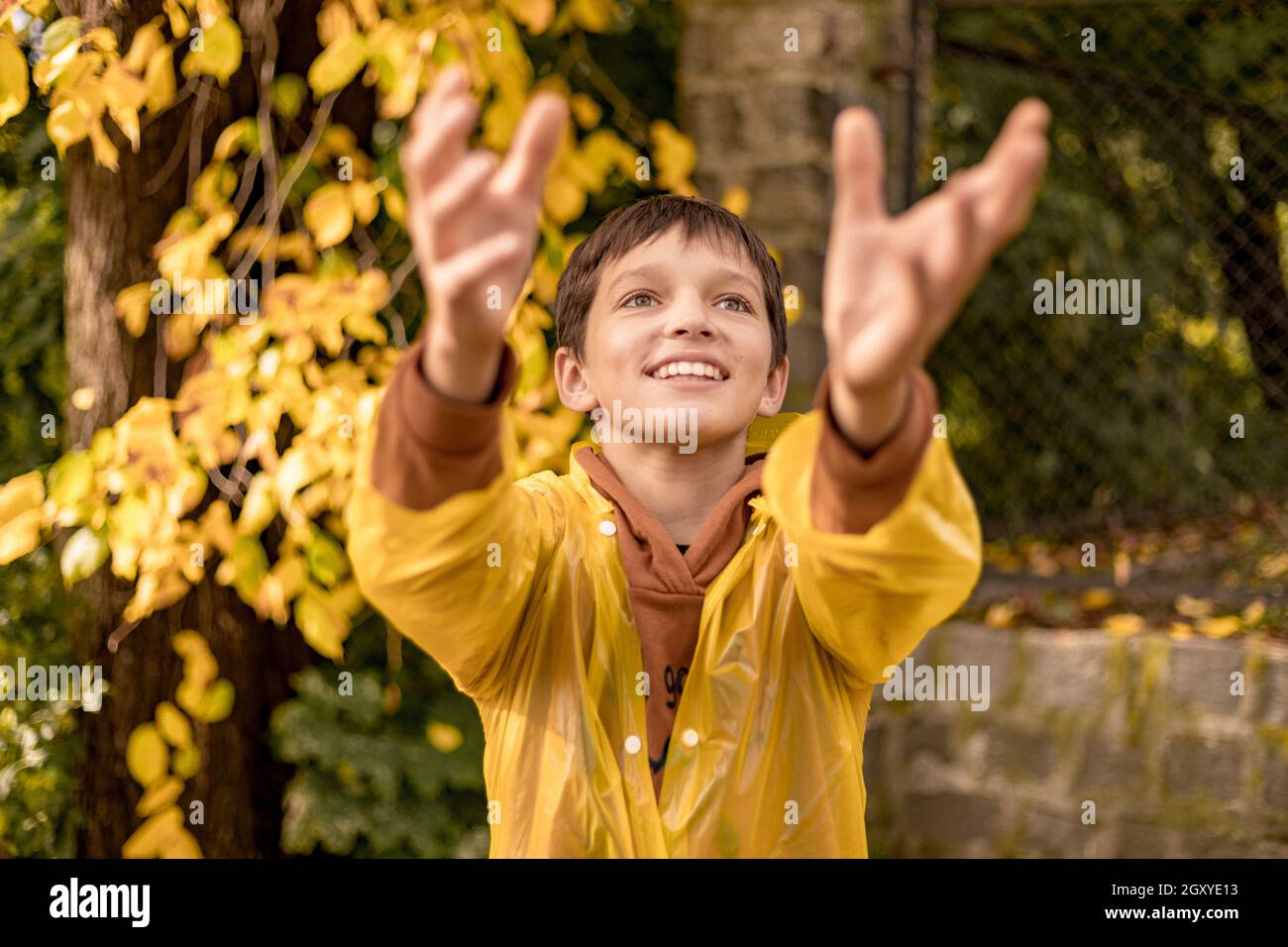 Photo d'adolescent dans un imperméable jaune parmi les feuilles d'automne, marche dans le parc de la ville, bonheur, rire Banque D'Images